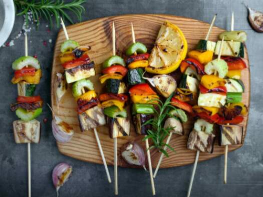 Colorful grilled summer seasonal vegetables skewers on rustic wooden board viewed from above