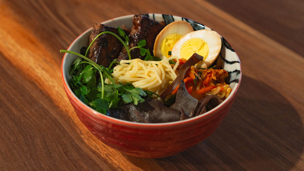 Image shows a bowl of food with eggs, noodles, meat, and vegetables.
