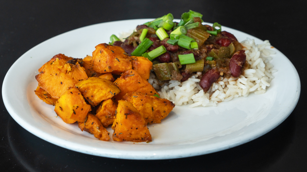 Image shows a plate of food: rice topped with beans and green onions and seasoned potatoes on the side.