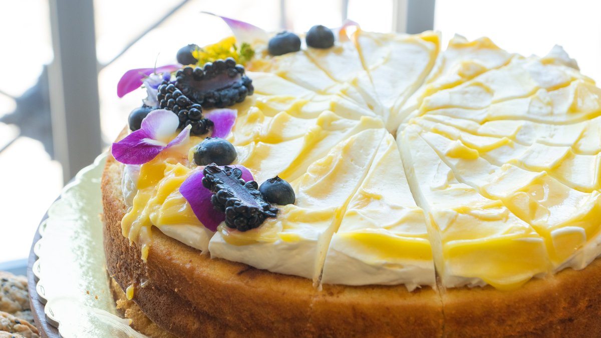 Image shows a close up for a cake with thick white meringue on top, decorated with blackberries, blueberries, and flowers.